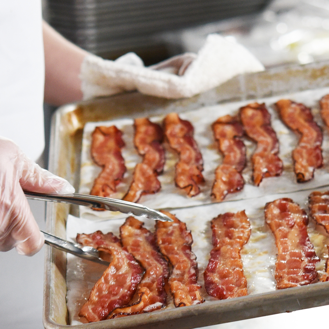 cooked bacon gathered on a baking sheet with tongs